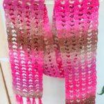 Handmade pink crochet scarves with fringes hanging.