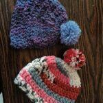 Two handmade knitted beanies with pom-poms on wood.