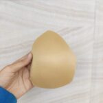 Hand holding a beige bra pad on wood background.