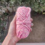 Hand holding pink and white yarn skein outdoors.