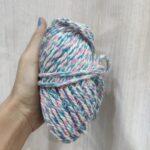 Hand holding multicolored twisted yarn ball.