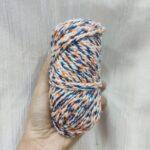 Multicolored yarn skein in hand against fabric background.