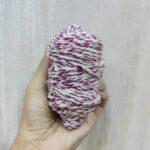 Hand holding purple and white twisted yarn skein.