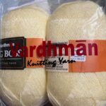 Two skeins of pale yellow knitting yarn in packaging.